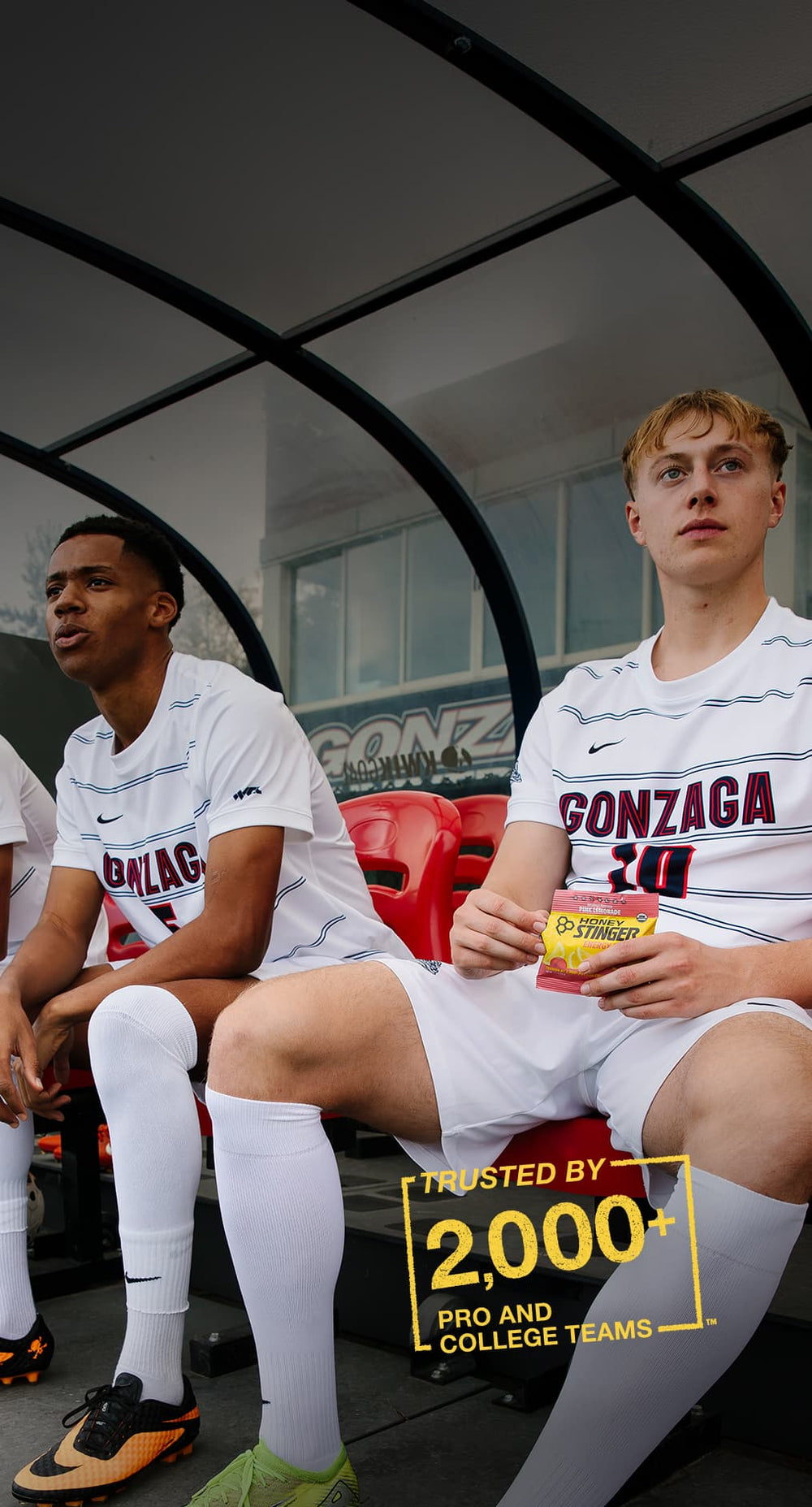 Two athletes in Gonzaga uniforms sitting on a bench eating Honey Stinger products - trusted by 2,000+ pro and college teams