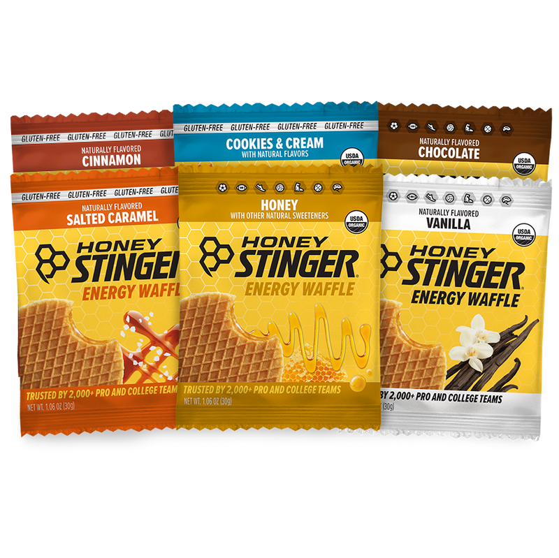 Six packages of Honey Stinger energy waffles in different flavors on a white background