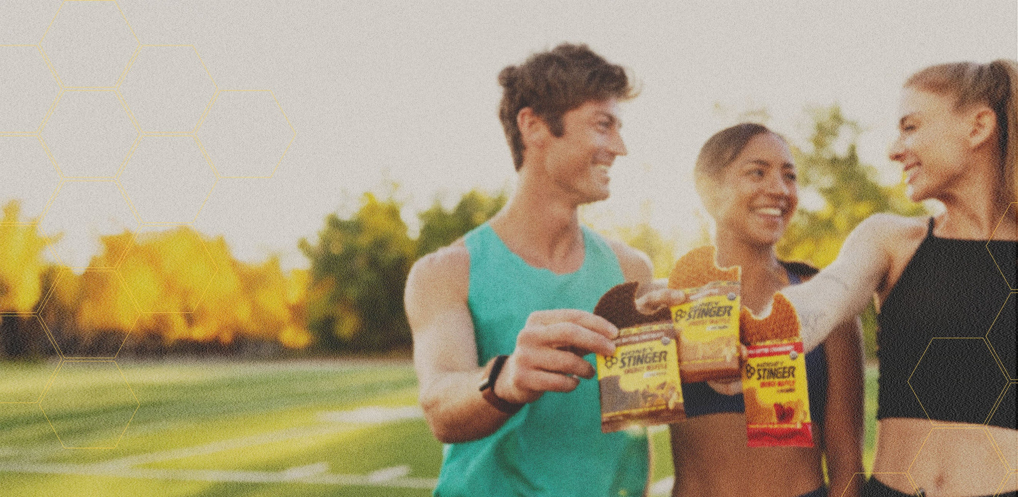 Three people outdoors holding Honey Stinger products with a scenic background