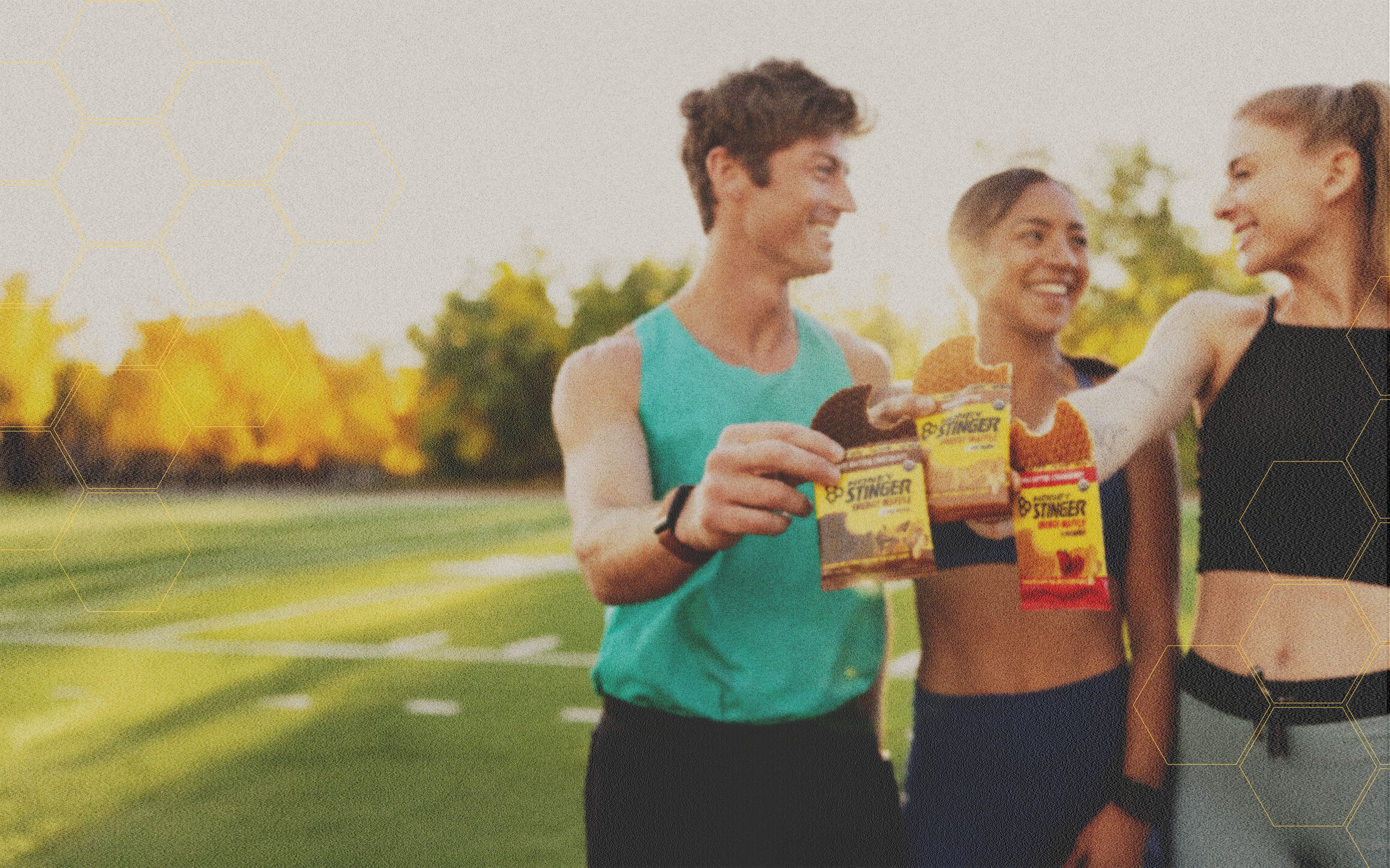 Three people outdoors holding Honey Stinger products with a scenic background
