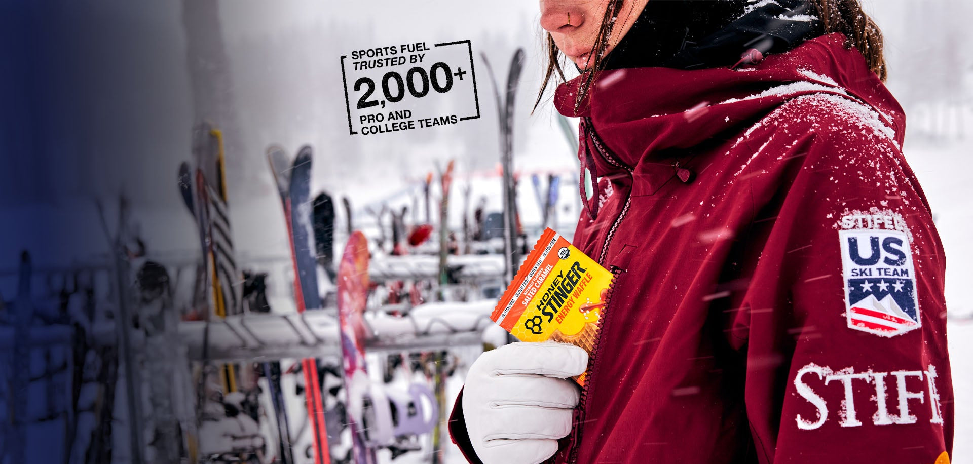 Person in red jacket holding a Honey Stinger Waffle with ski equipment in the background