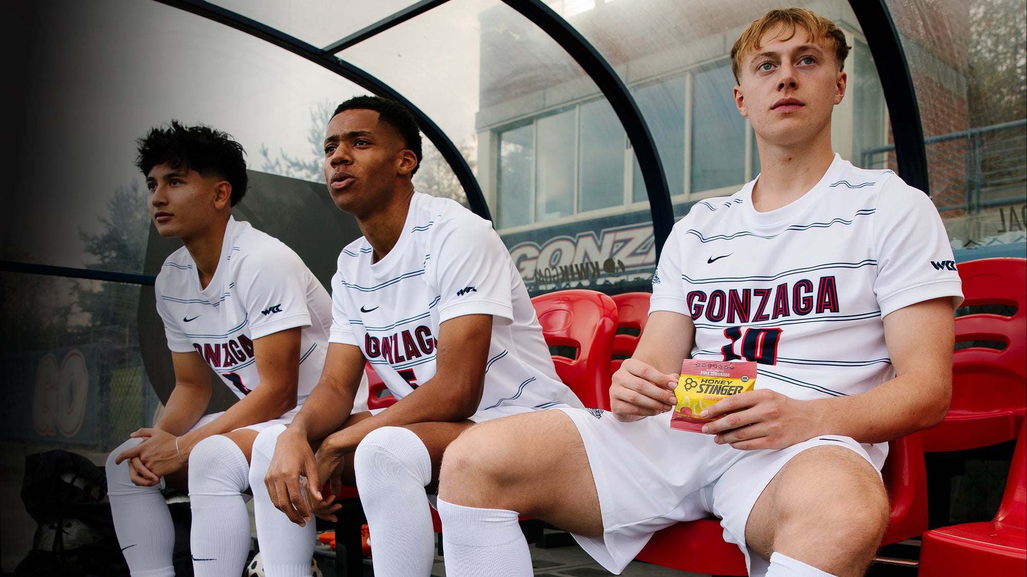 Three young men sitting on a bench with sports jerseys and Gonzaga branding.